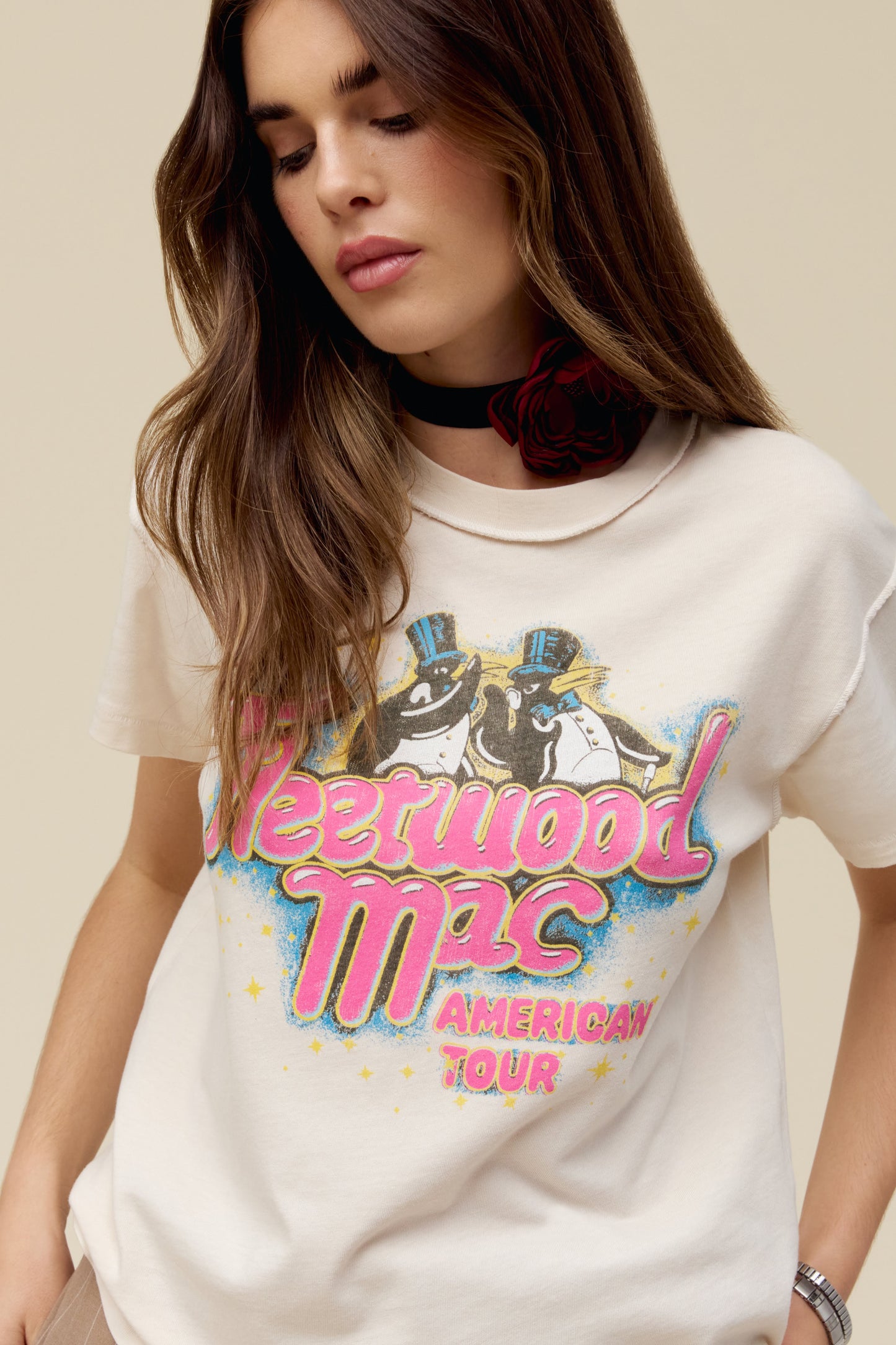 A model featuring a dirty white Fleetwood Mac tour tee designed with with their group name and a penguin graphic; with a special shoutout to their American Tour featuring their city stops stamped on the back.