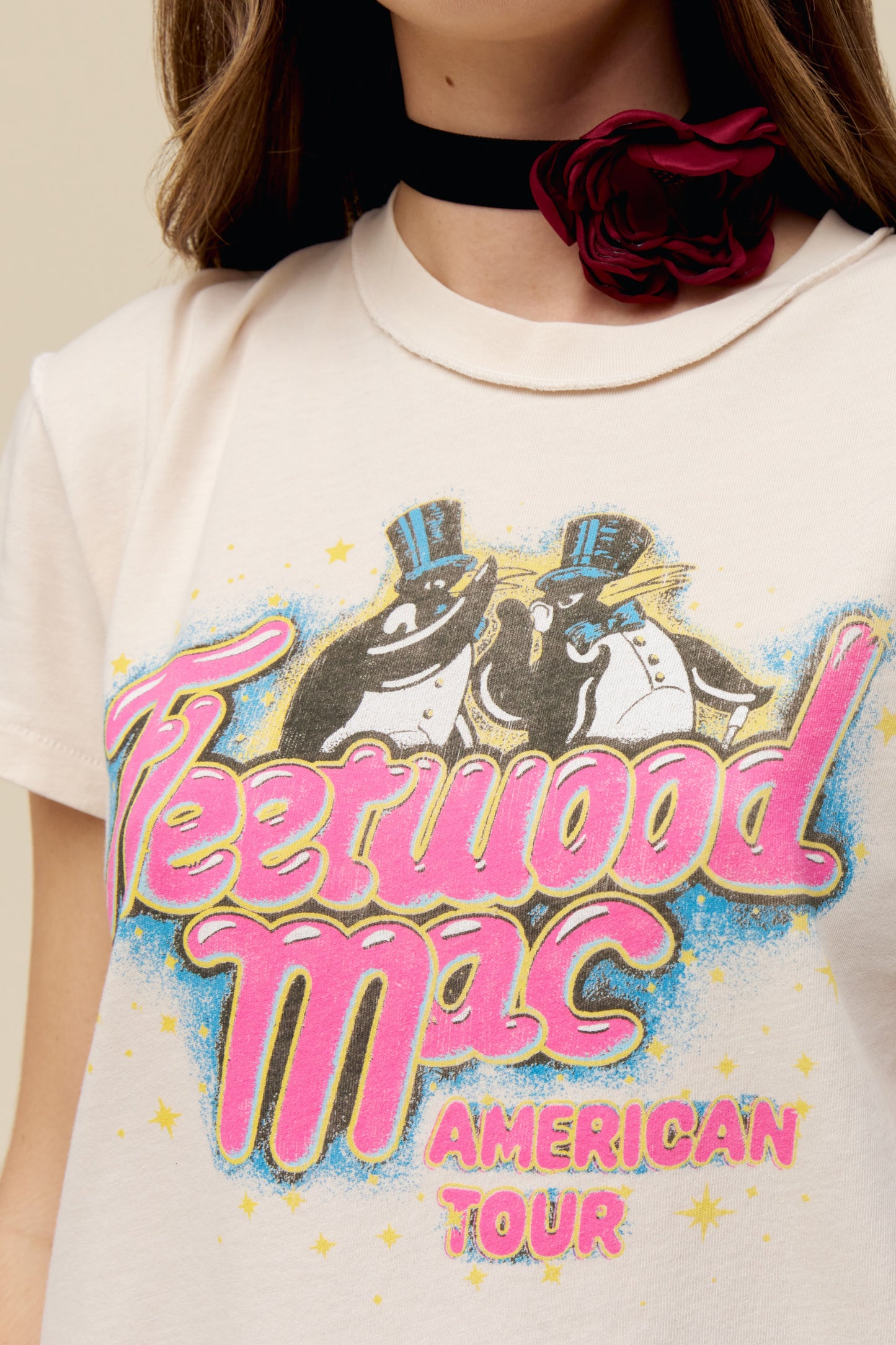 A model featuring a dirty white Fleetwood Mac tour tee designed with with their group name and a penguin graphic; with a special shoutout to their American Tour featuring their city stops stamped on the back.