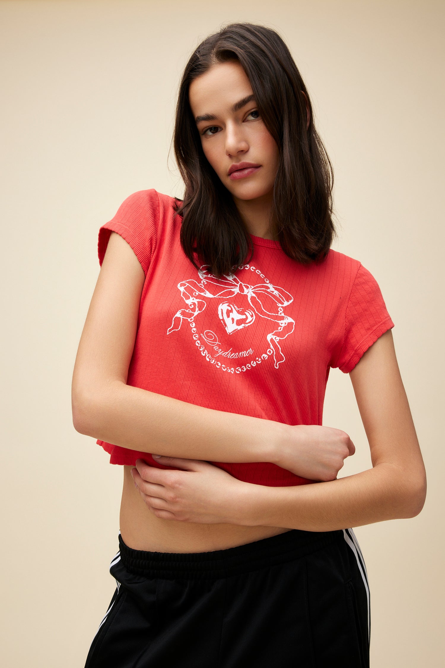 Model wearing a red pointelle baby tee with a bow graphic and 'Daydreamer' logo script on the front.