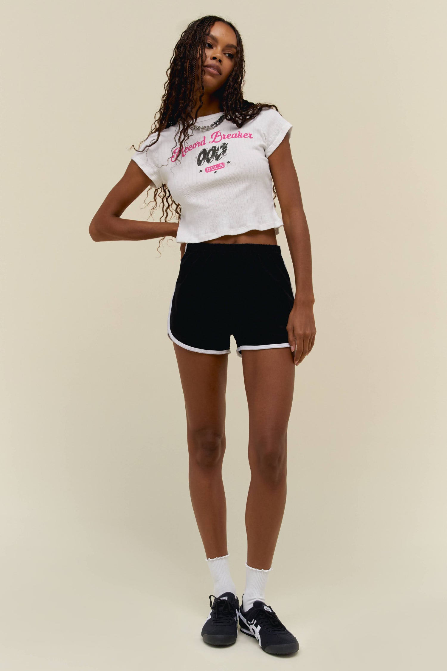 Model wearing a pointelle baby tee with contrast pink 'Record Breaker' and 'DDLA' logo graphics on the front.