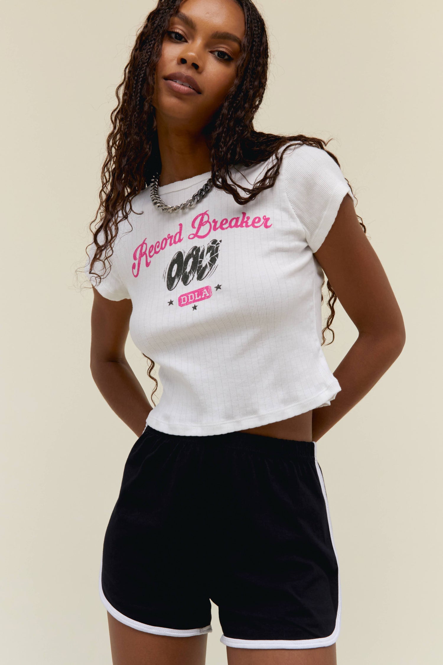 Model wearing a pointelle baby tee with contrast pink 'Record Breaker' and 'DDLA' logo graphics on the front.