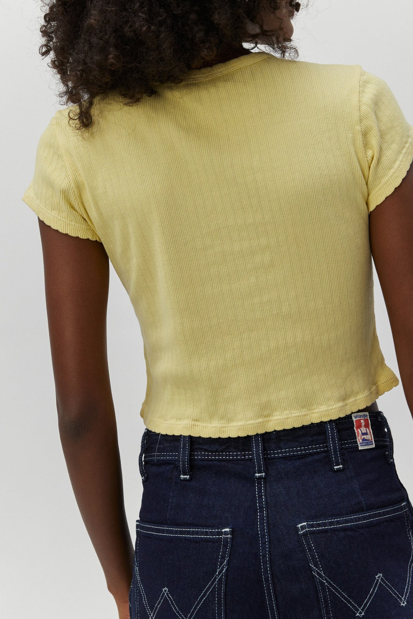 Curly haired model wearing a pointelle knit crop tee in yellow.