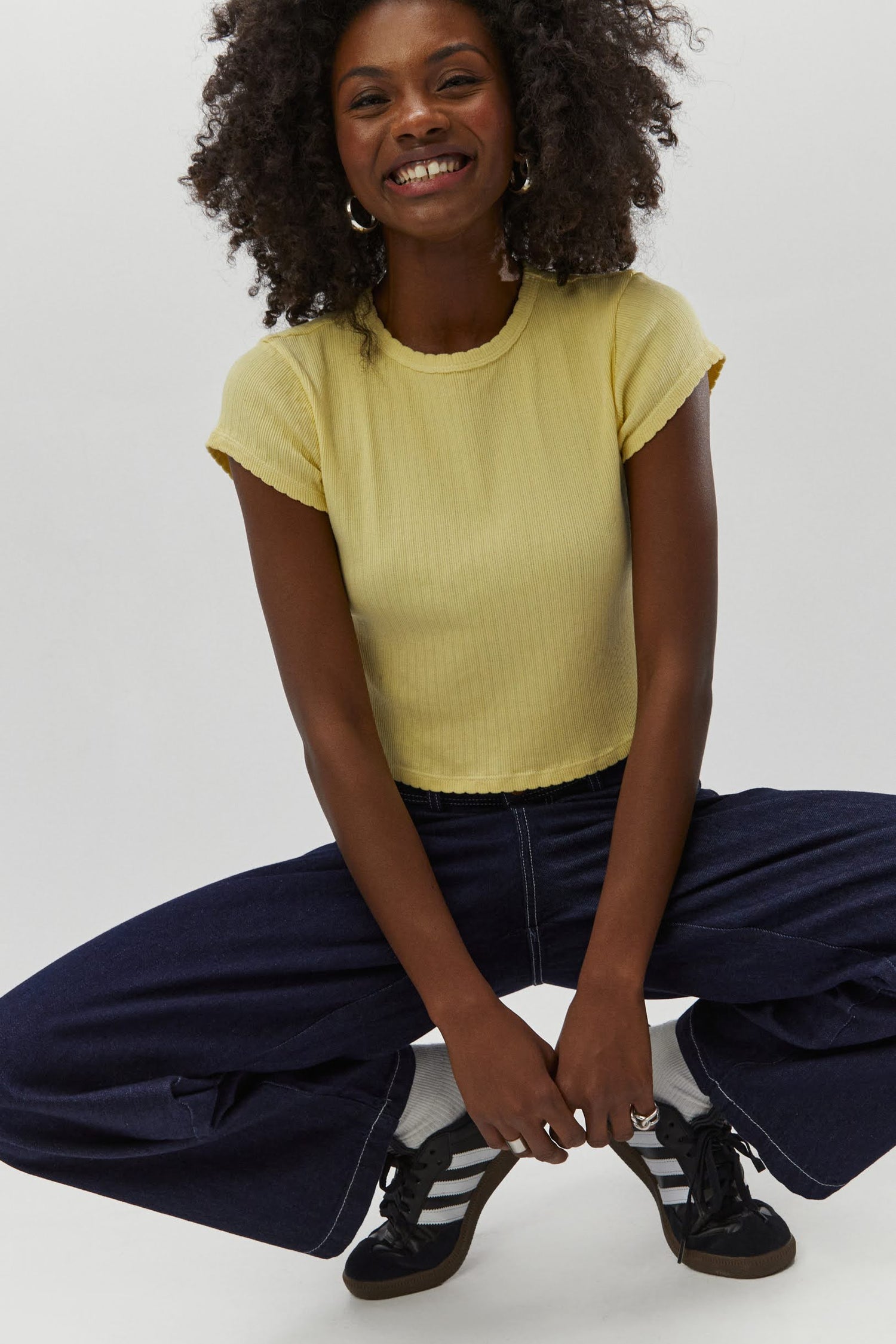 Curly haired model wearing a pointelle knit crop tee in yellow.