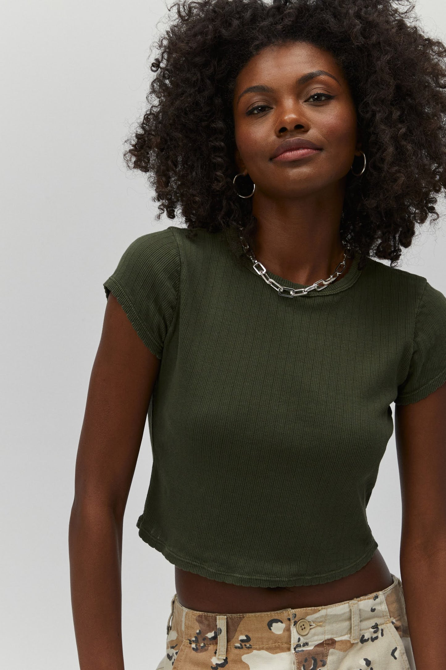 Curly haired model wearing a pointelle knit crop tee in military green.