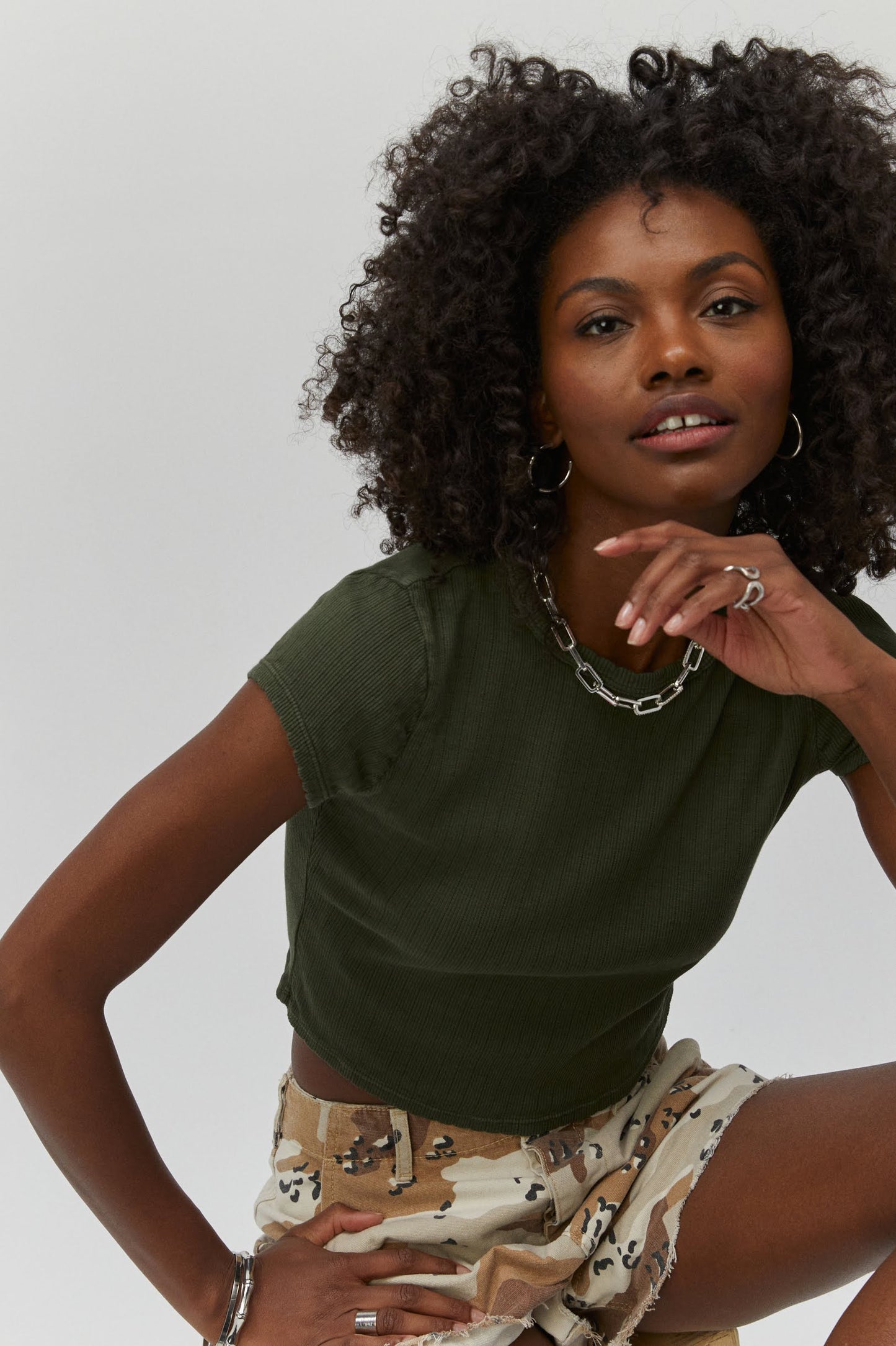 Curly haired model wearing a pointelle knit crop tee in military green.