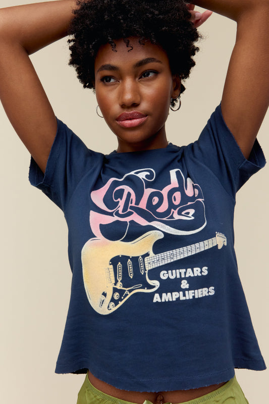 A model featuring a navy tee stamped with red, guitars, & amplifiers and a graphic of a guitar on the middle.