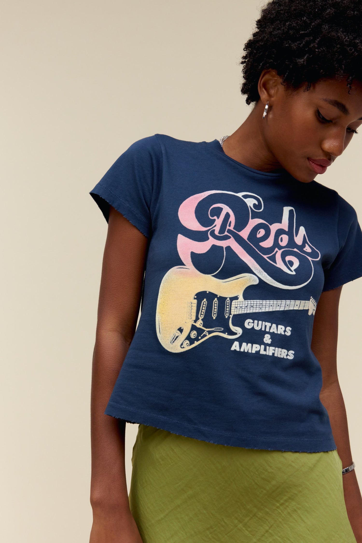 A model featuring a navy tee stamped with red, guitars, & amplifiers and a graphic of a guitar on the middle.