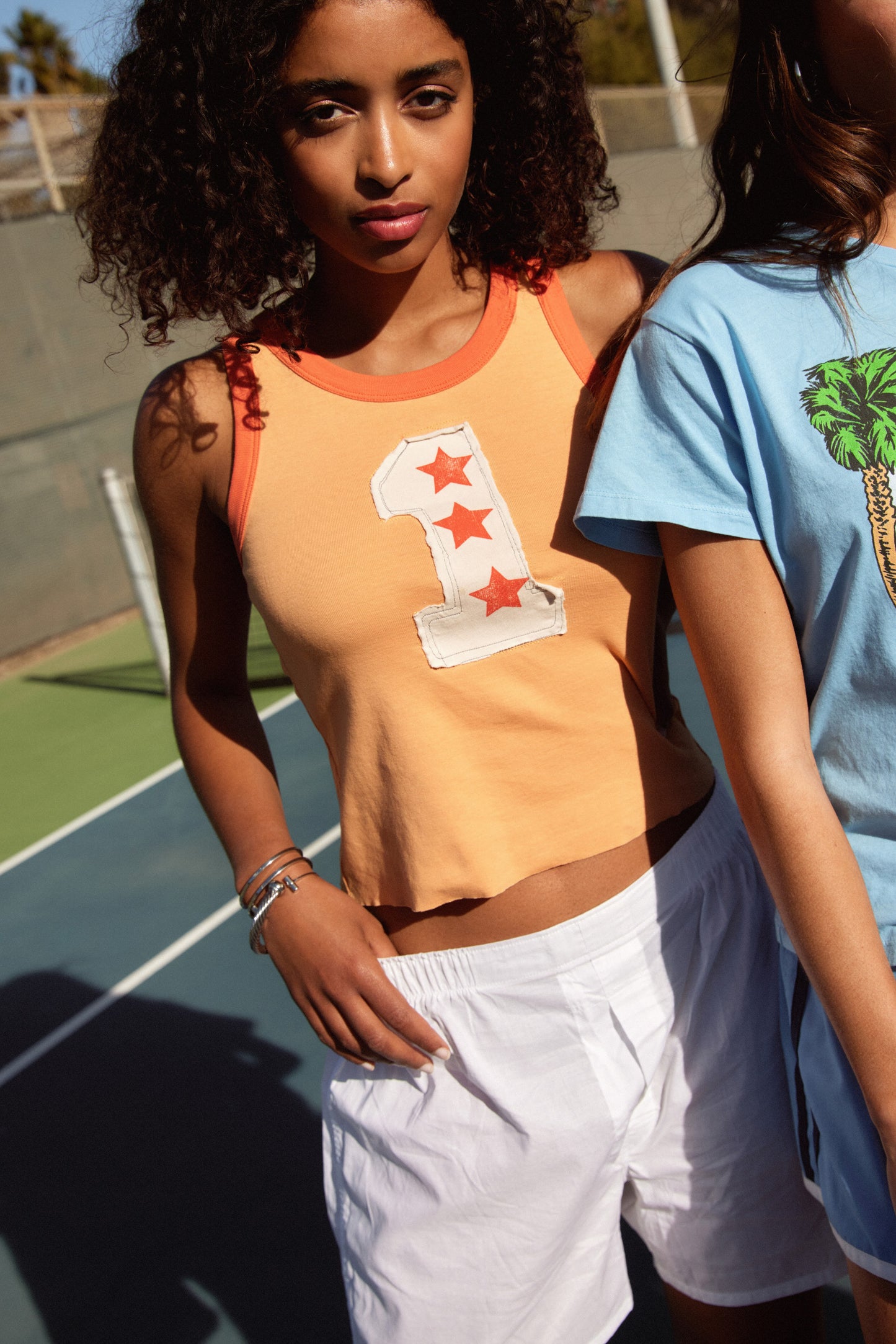 A model featuring an orange racer tank designed with a one with three stars.