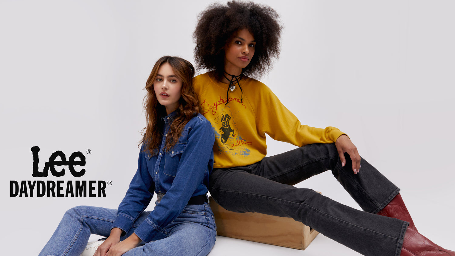 two models sitting - one wearing a denim butotn up shirt and the other in black jeans and a marigold crewneck
