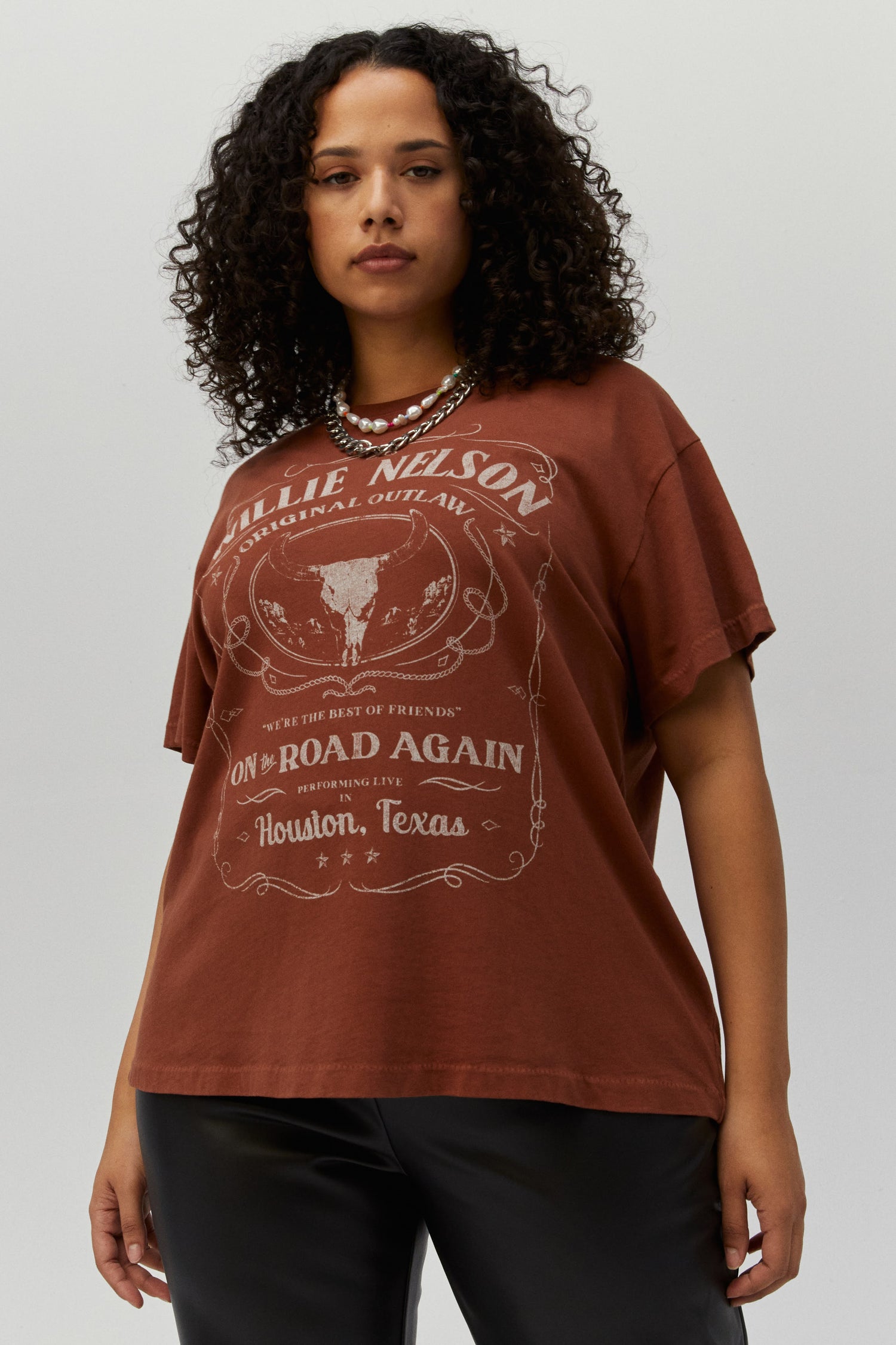 Dark curly-haired plus size model featuring a sable tee designed with a stamped lyric from his hit country track “On the Road Again,” this is a true graphic fit to represent the legend who spearheaded the outlaw music movement.