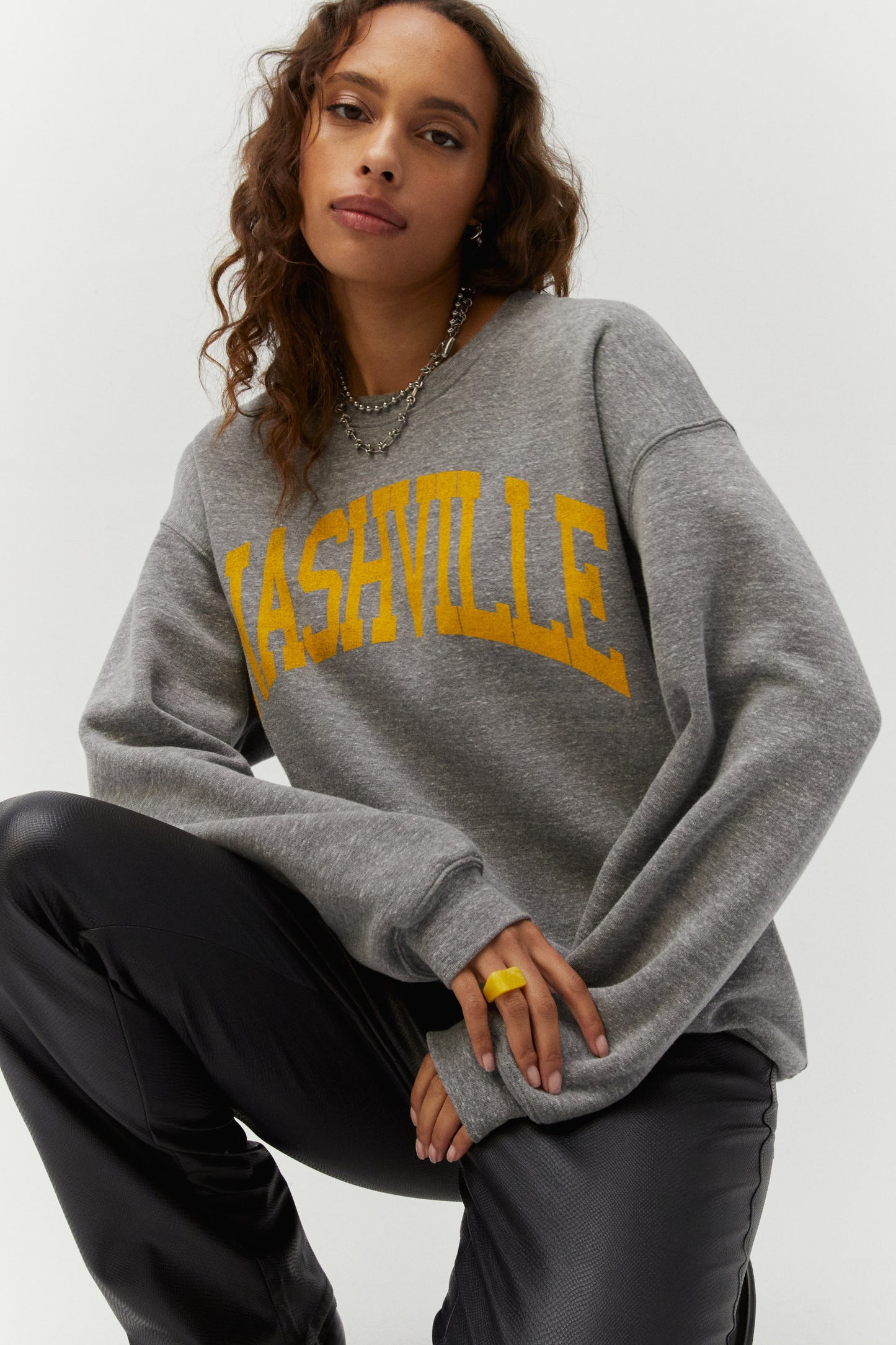 Brown curly-haired model featuring a gray crew designed with ‘Nashville’ in collegiate style letters