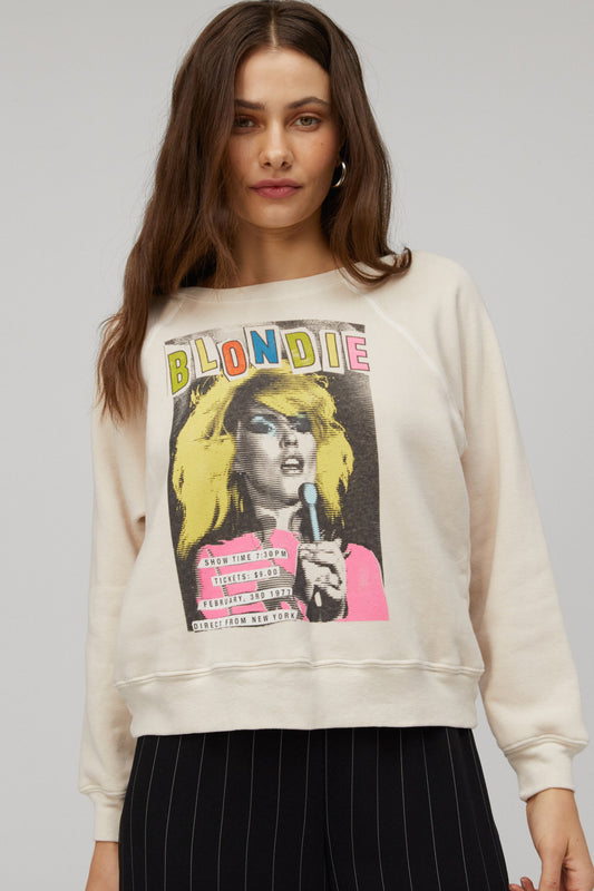Brown-haired model featuring a dirty white crew with a portrait of Debbie Harry, an artsy large font "BLONDIE" in different colors, and a schedule of the show at the bottom left