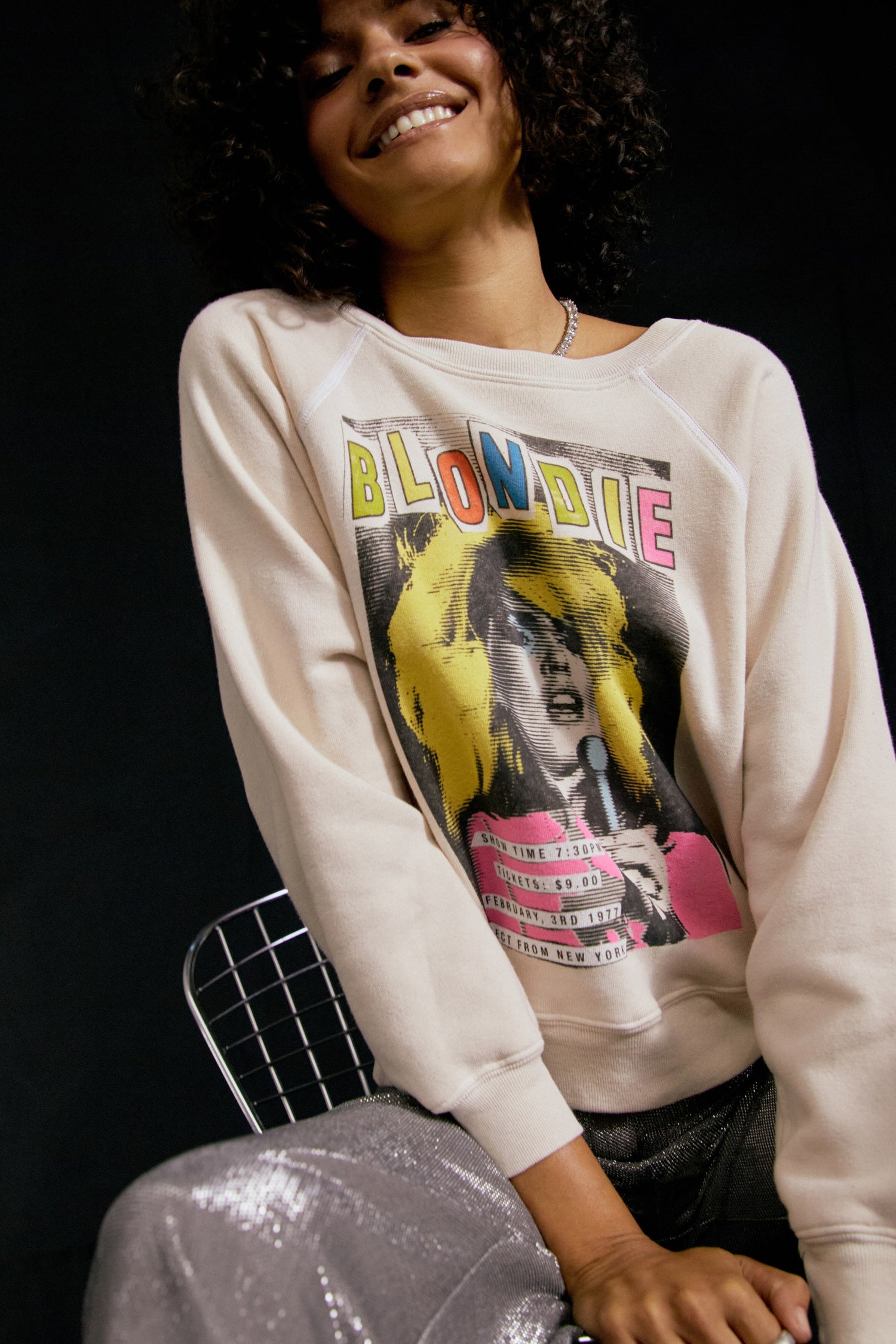 Dark curly-haired model featuring a dirty white crew with a portrait of Debbie Harry, an artsy large font "BLONDIE" in different colors, and a schedule of the show at the bottom left