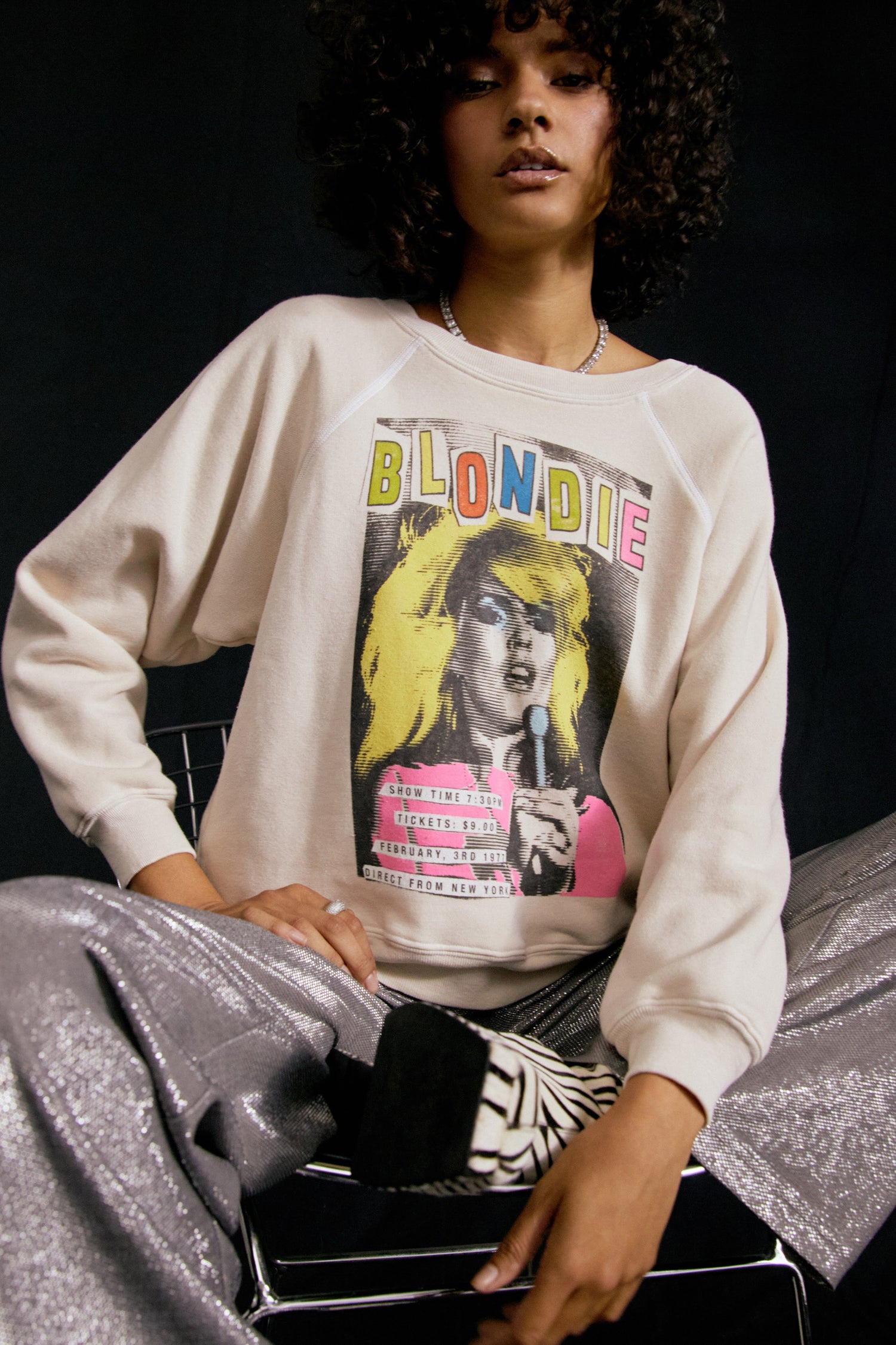 Dark curly-haired model featuring a dirty white crew with a portrait of Debbie Harry, an artsy large font "BLONDIE" in different colors, and a schedule of the show at the bottom left