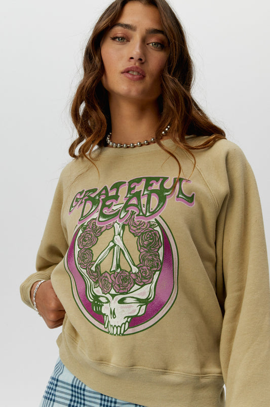 A brown curly-haired model wearing a khaki tee featuring a hand-drawn rendition of a skull and roses graphic is the lead focal point, accented with the group’s logo in trippy letters and a pop of pink