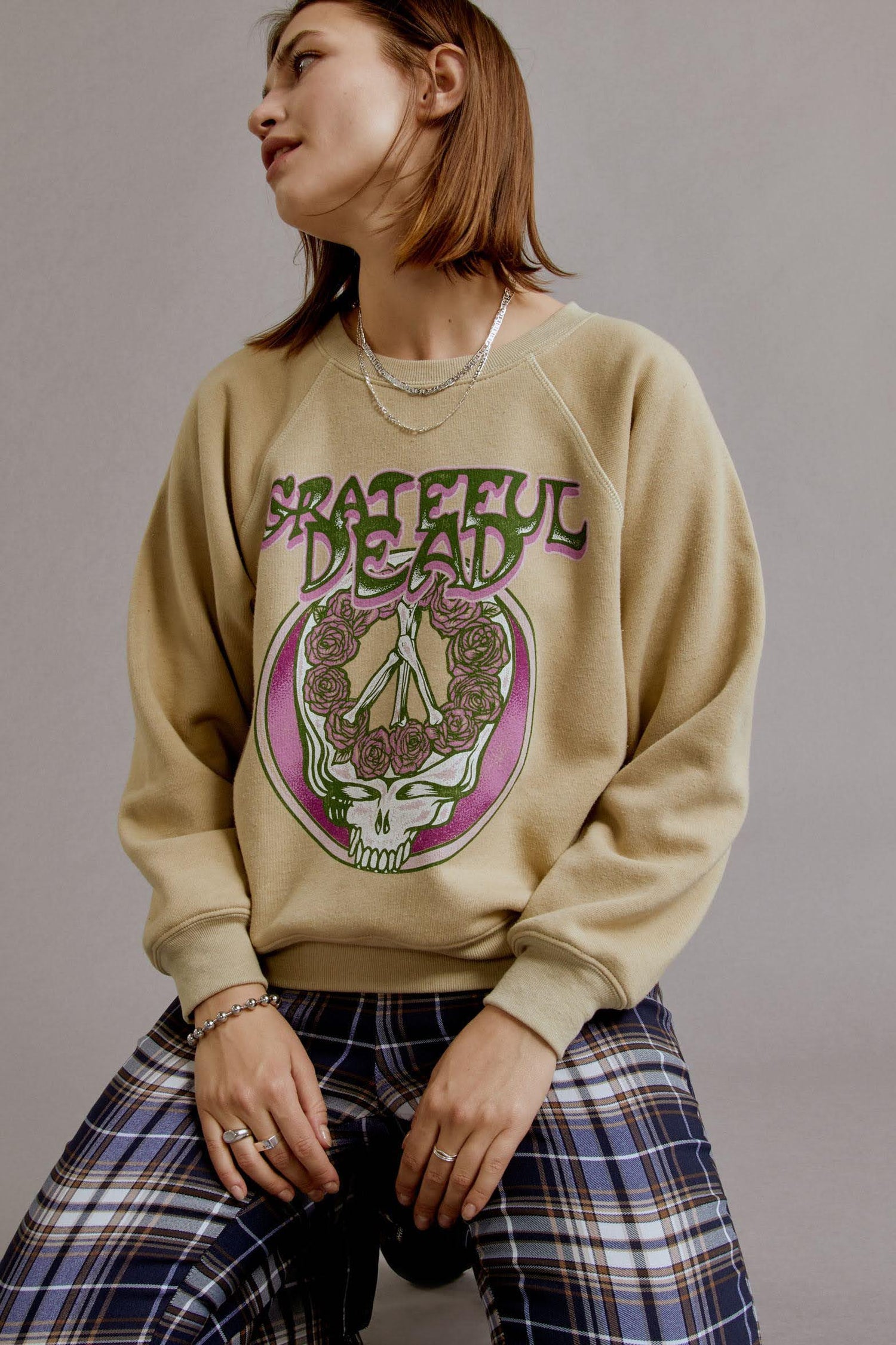 A brown-haired model wearing a khaki tee featuring a hand-drawn rendition of a skull and roses graphic is the lead focal point, accented with the group’s logo in trippy letters and a pop of pink