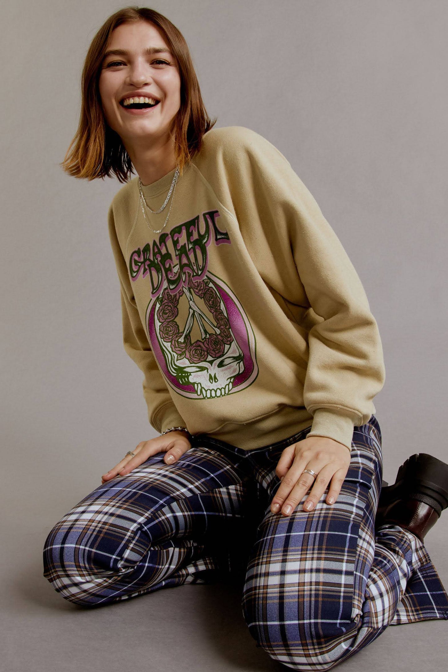 A brown-haired model wearing a khaki tee featuring a hand-drawn rendition of a skull and roses graphic is the lead focal point, accented with the group’s logo in trippy letters and a pop of pink