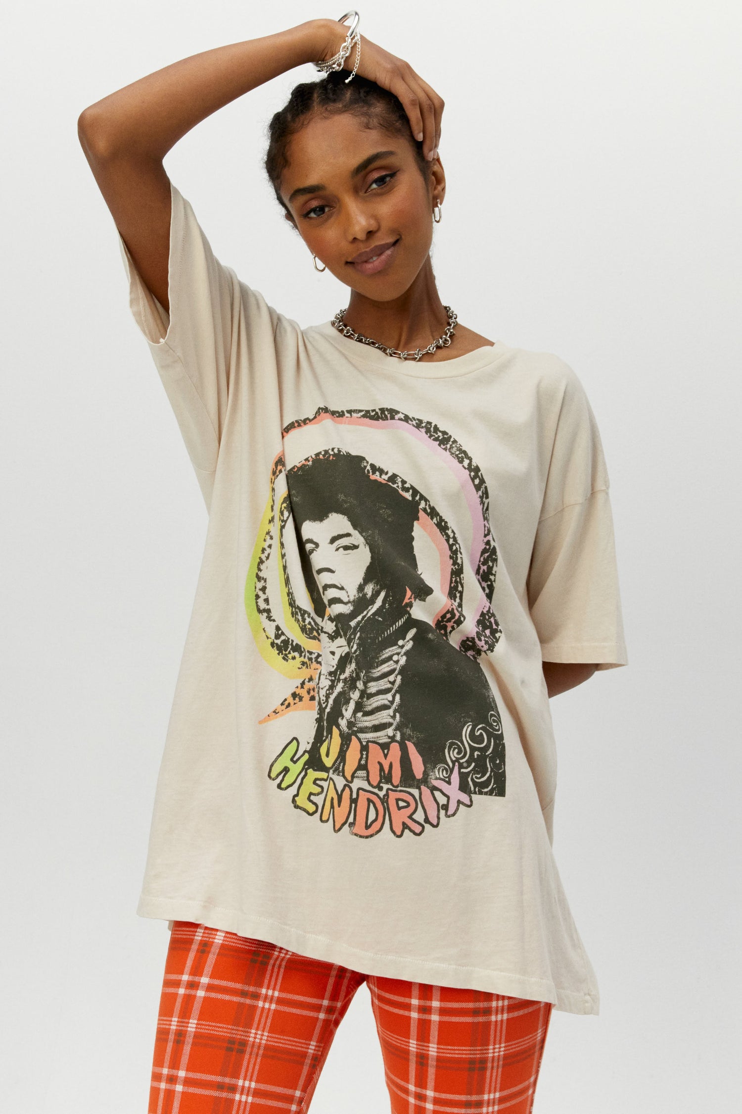 Dark braided-haired model featuring a dirty white tee designed with a multi-colored spiral with the icon’s portrait and name in hand-drawn letters