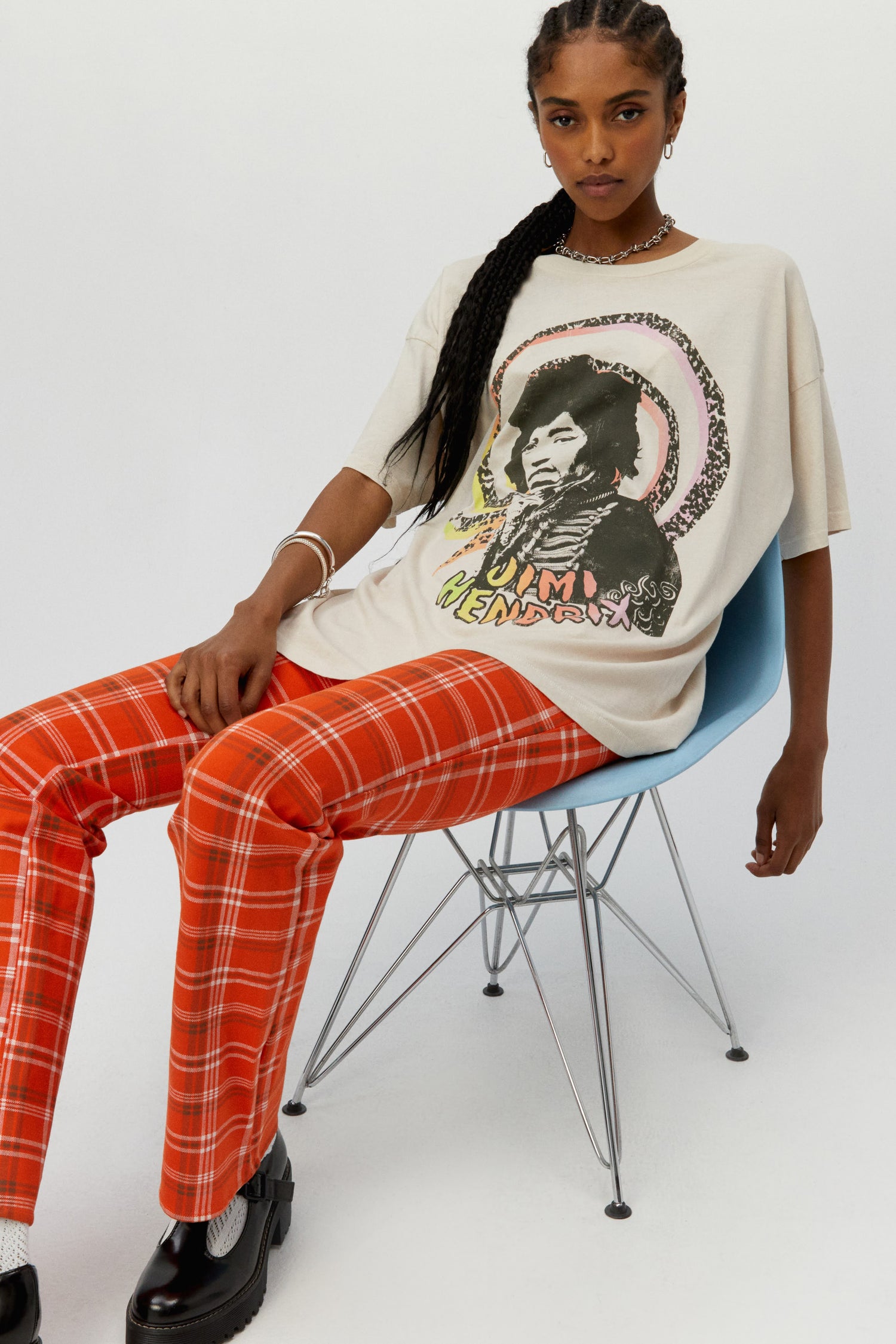 Dark braided-haired model featuring a dirty white tee designed with a multi-colored spiral with the icon’s portrait and name in hand-drawn letters