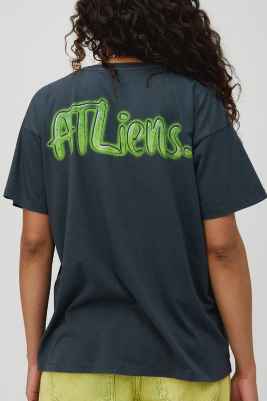 Dark curly-haired model wearing a black tee designed with the boy's center chest and ATLiens featured on the back