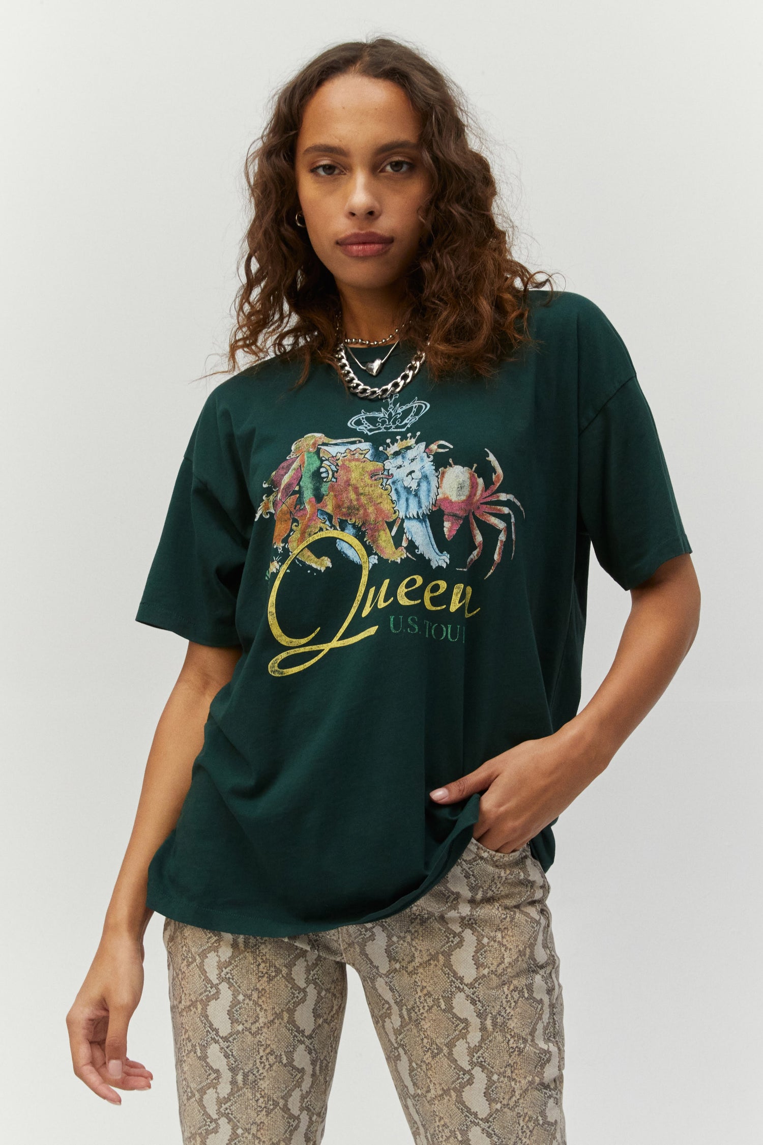 Dark curly-haired model featuring an emerald-colored tee designed with the art of royalty status, pops of color, and a slap of their logo